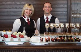 Two servers standing in front of many delicious desserts.
