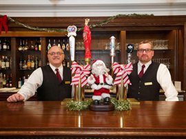 Two servers smiling behind the bar, with Christmas decorations.